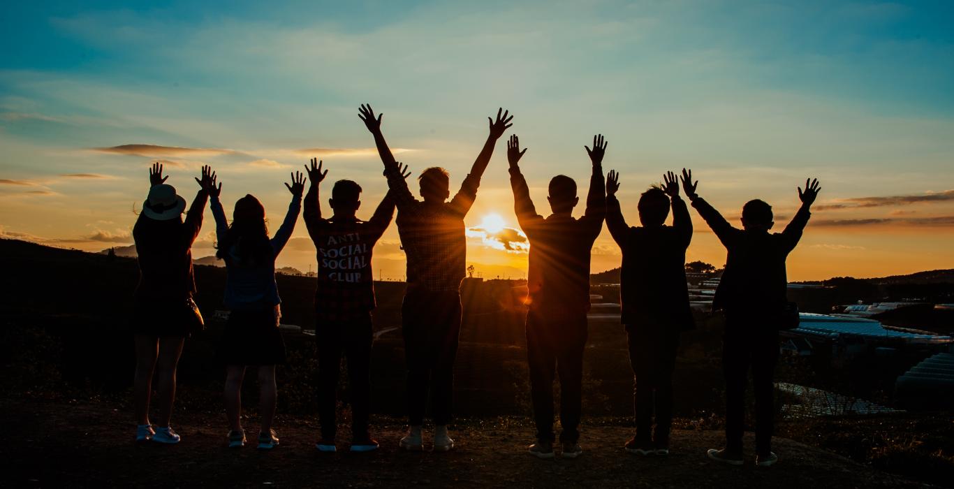  Silhouette d'un groupe de personnes avec leurs bras levés en regardant le coucher du soleil
