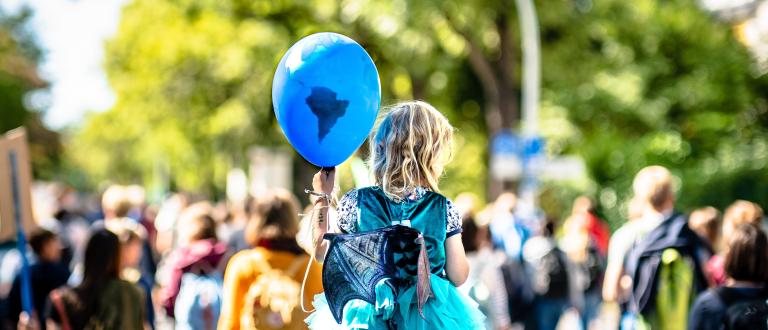 Little girl in a crowd holding a blue, planet earth balloon