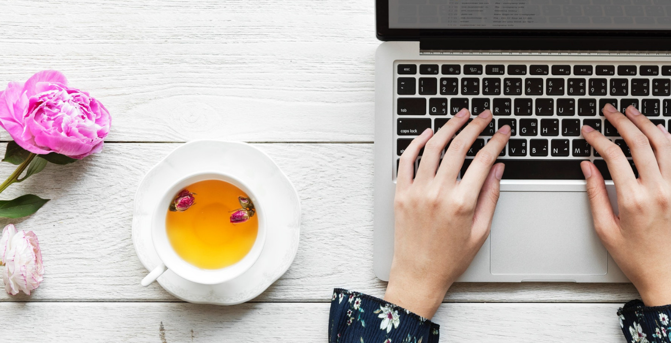  Image de mains de femme tapant sur un ordinateur portable à côté d'une tasse de thé et de fleurs