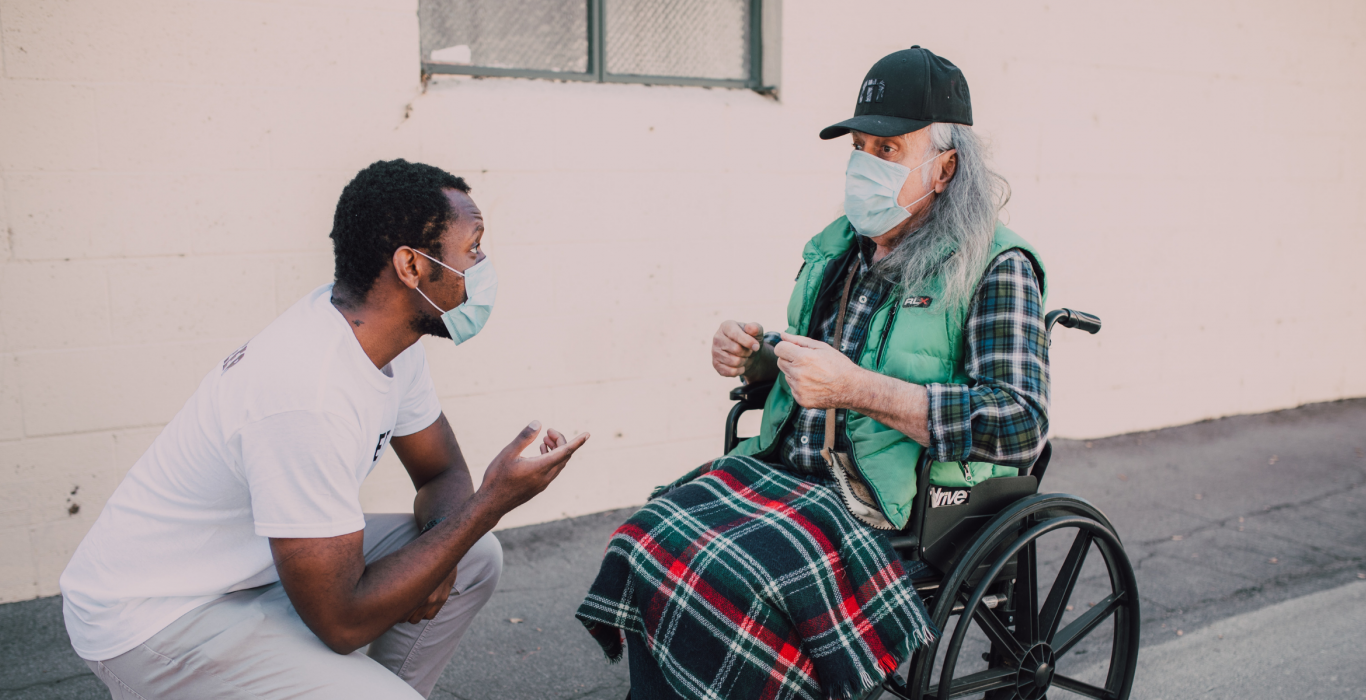 Man helping another man in wheelchair