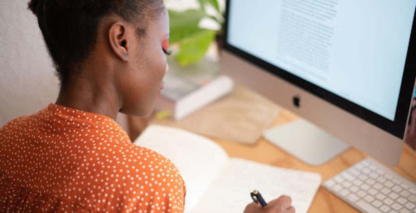 Photo: black woman in orange shirt writing in a notebook
