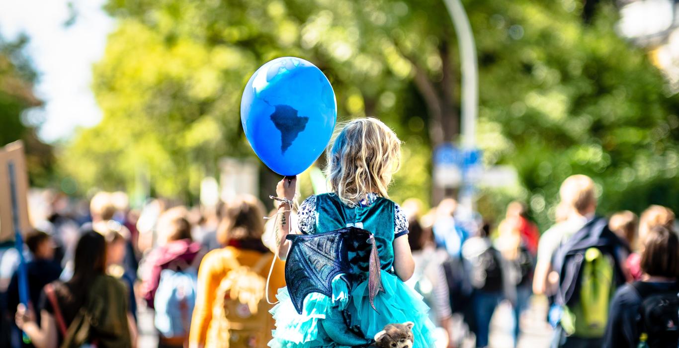 Little girl in a crowd holding a blue, planet earth balloon