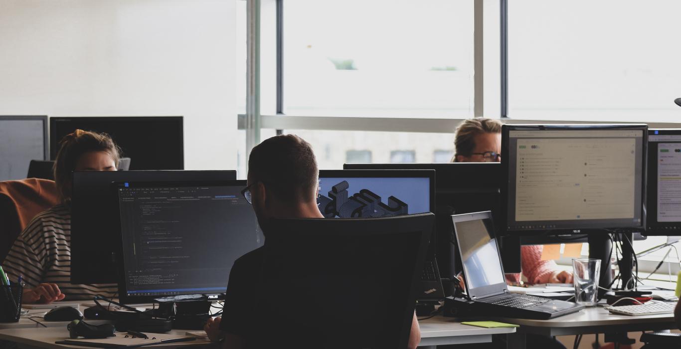 photo of office, computers, displays, monitors and a few people working in front of computers.